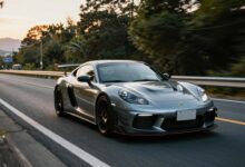 Carro esportivo em uma estrada japonesa ao pôr do sol, com montanhas, cidade iluminada e atmosfera de festival automotivo