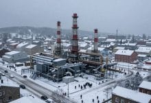Cidade de Frostpunk 2 em meio a uma tempestade de neve, com um grande gerador, distritos industriais e sobreviventes reunidos