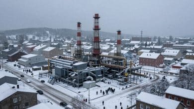 Cidade de Frostpunk 2 em meio a uma tempestade de neve, com um grande gerador, distritos industriais e sobreviventes reunidos