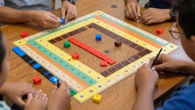 Mesa de Rummikub vista de cima, com peças coloridas formando sequências e grupos, destacando estratégia e competição entre jogadores